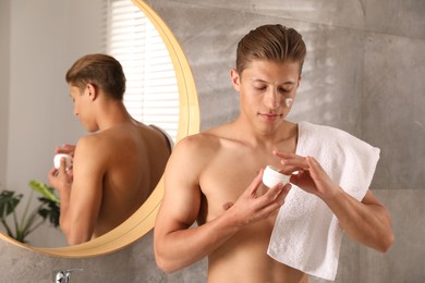 Photo of Handsome young man with jar of face cream in bathroom