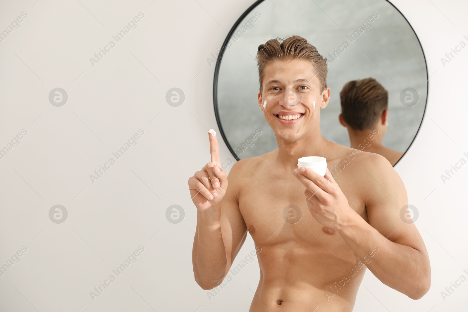 Photo of Handsome young man with jar of face cream near mirror at home, space for text