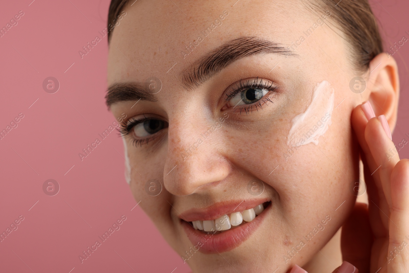 Photo of Beautiful woman with cream on her face against pink background, closeup