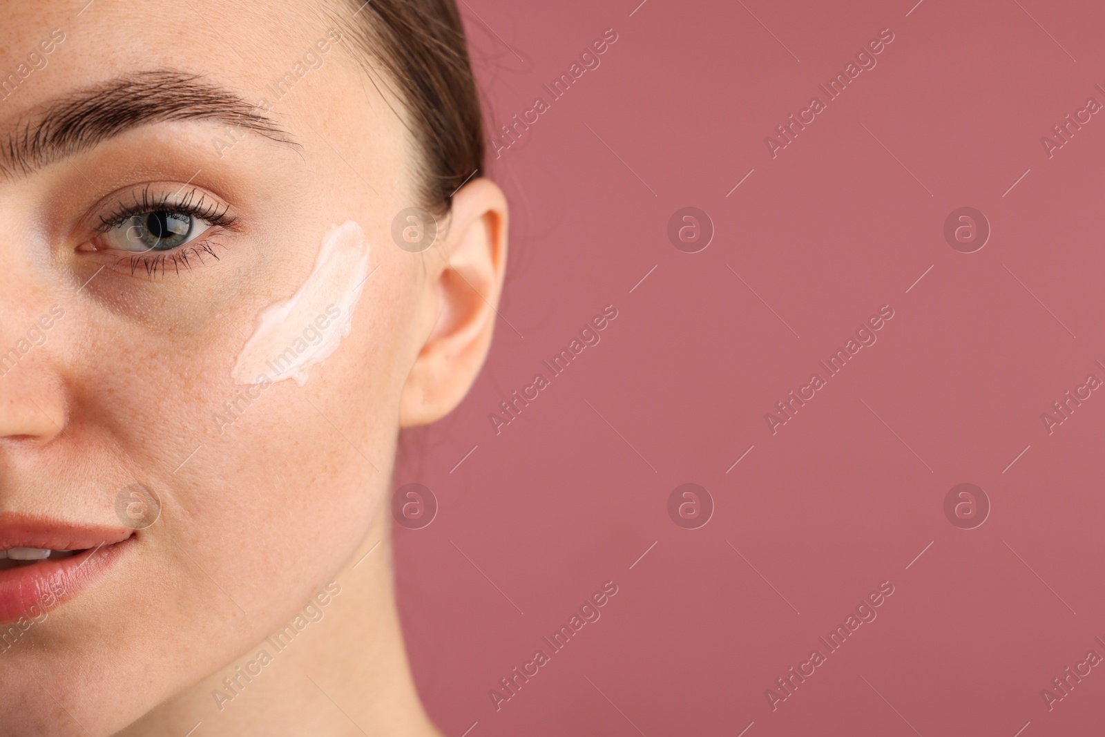 Photo of Beautiful woman with cream on her face against pink background, closeup. Space for text
