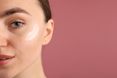 Photo of Beautiful woman with cream on her face against pink background, closeup. Space for text