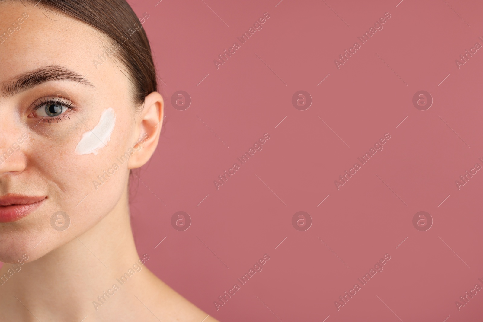 Photo of Beautiful woman with cream on her face against pink background, closeup. Space for text