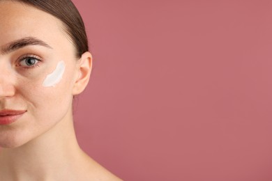 Photo of Beautiful woman with cream on her face against pink background, closeup. Space for text