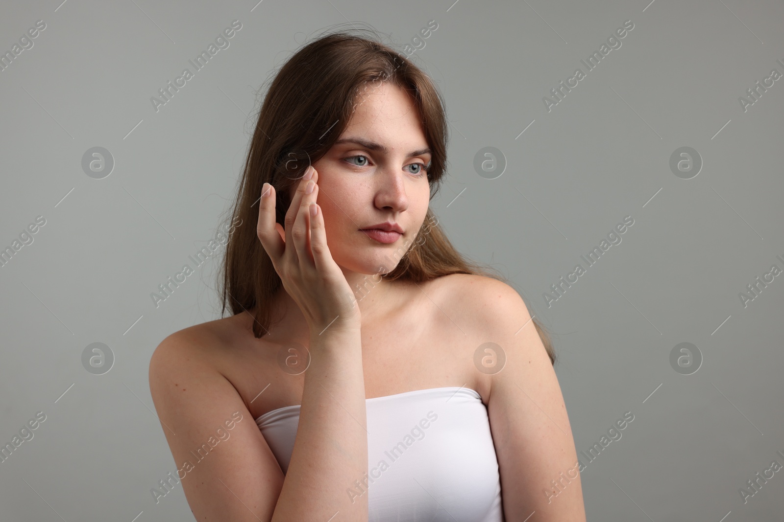 Photo of Beautiful woman applying cream onto her face on gray background