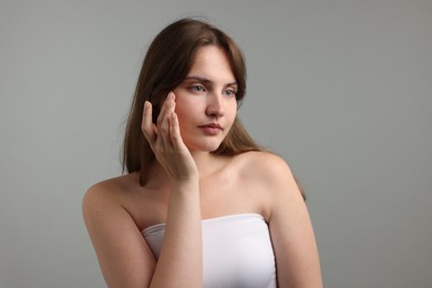Photo of Beautiful woman applying cream onto her face on gray background