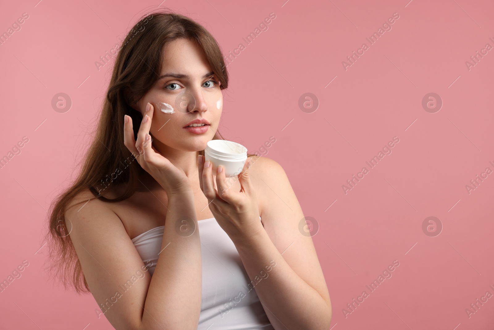 Beautiful woman applying cream onto her face on pink background. Space for text Photo of Beautiful woman applying cream onto her face on pink background. Space for text