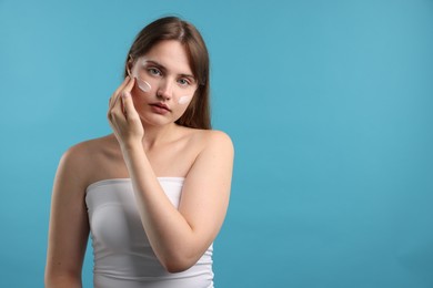 Photo of Beautiful woman applying cream onto her face on light blue background. Space for text