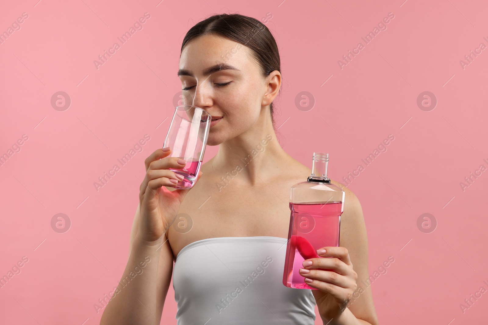Photo of Woman rinsing mouth with mouthwash on pink background. Oral hygiene