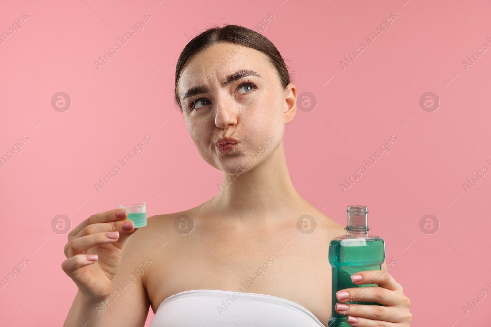 Photo of Woman rinsing mouth with mouthwash on pink background. Oral hygiene