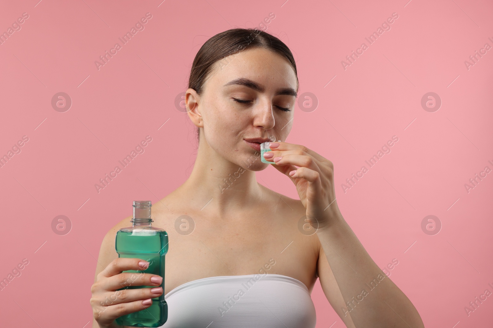 Photo of Woman rinsing mouth with mouthwash on pink background. Oral hygiene