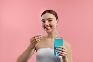 Photo of Woman with bottle and cap of mouthwash on pink background. Oral hygiene