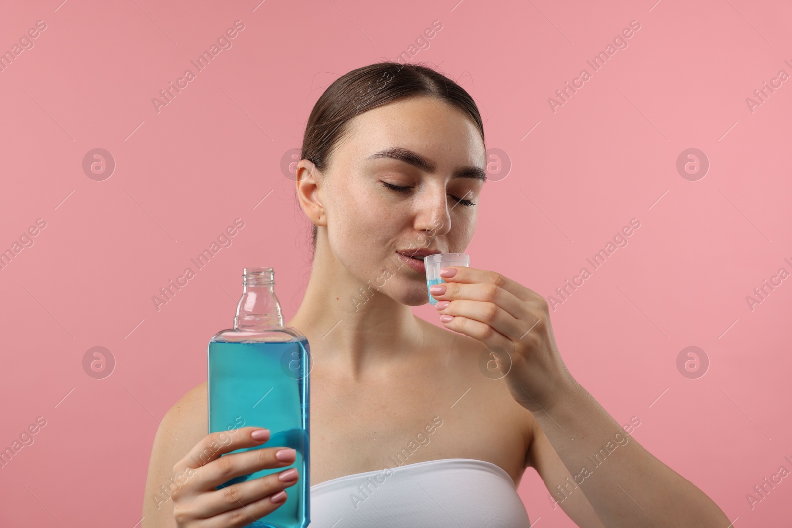 Photo of Woman rinsing mouth with mouthwash on pink background. Oral hygiene
