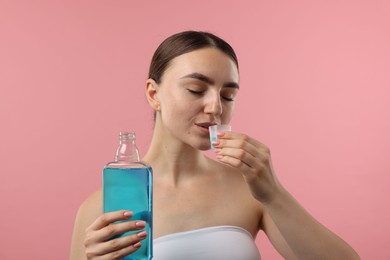Photo of Woman rinsing mouth with mouthwash on pink background. Oral hygiene