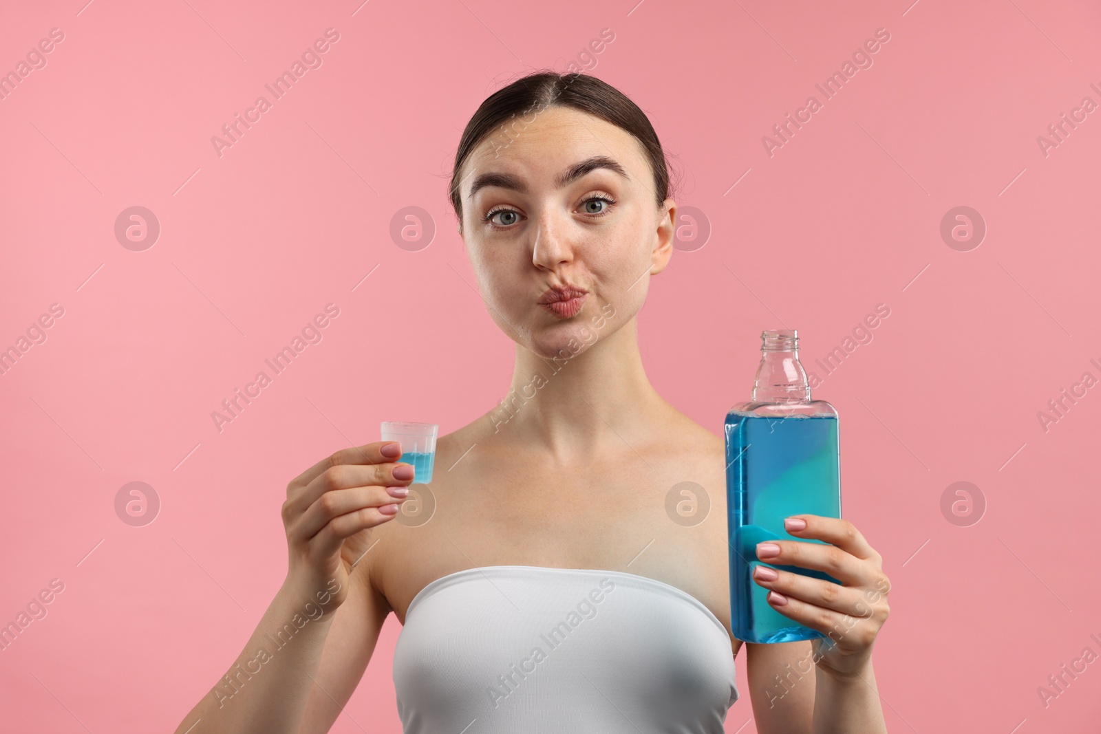 Photo of Woman rinsing mouth with mouthwash on pink background. Oral hygiene
