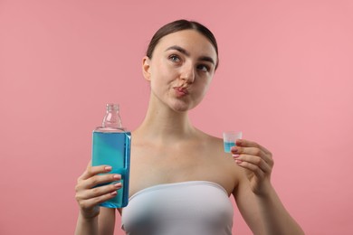 Photo of Woman rinsing mouth with mouthwash on pink background. Oral hygiene