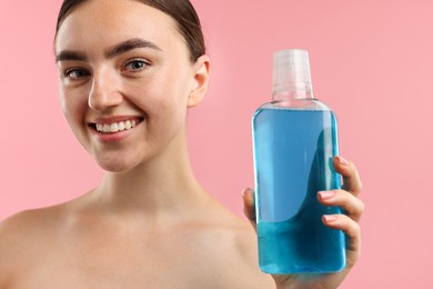 Photo of Woman with bottle of mouthwash on pink background, closeup. Oral hygiene