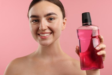 Photo of Woman with bottle of mouthwash on pink background, closeup. Oral hygiene
