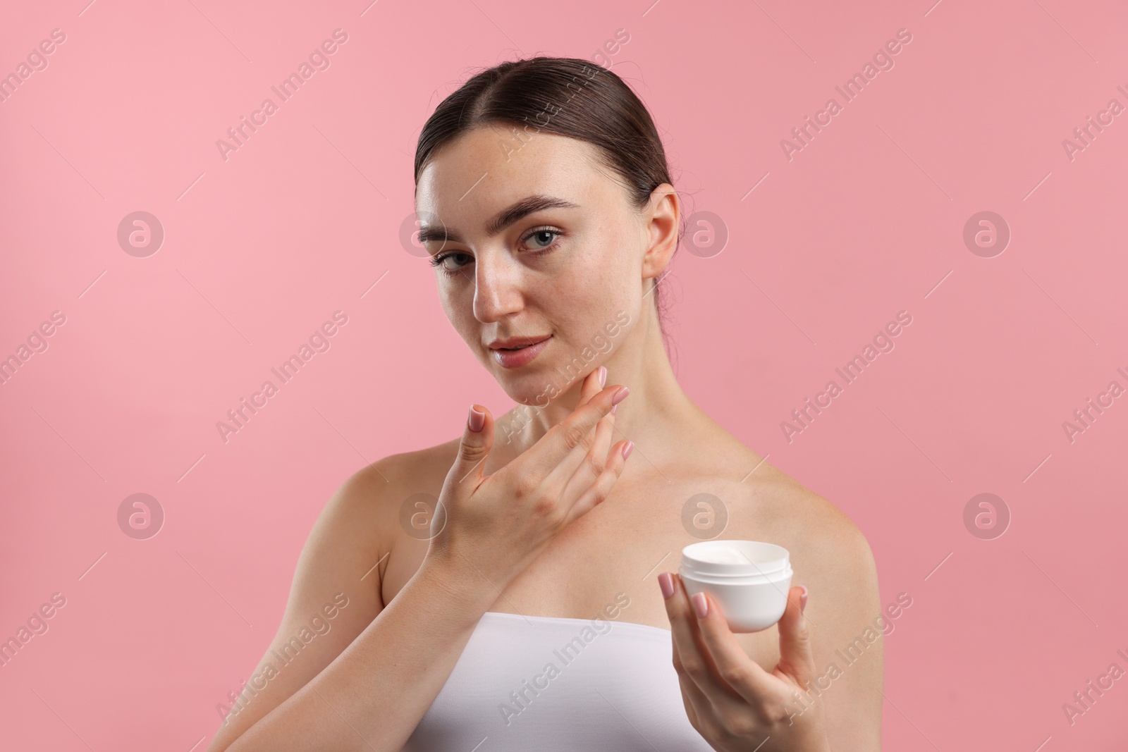 Photo of Beautiful woman applying cream onto her face on pink background