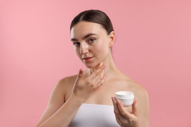 Photo of Beautiful woman applying cream onto her face on pink background