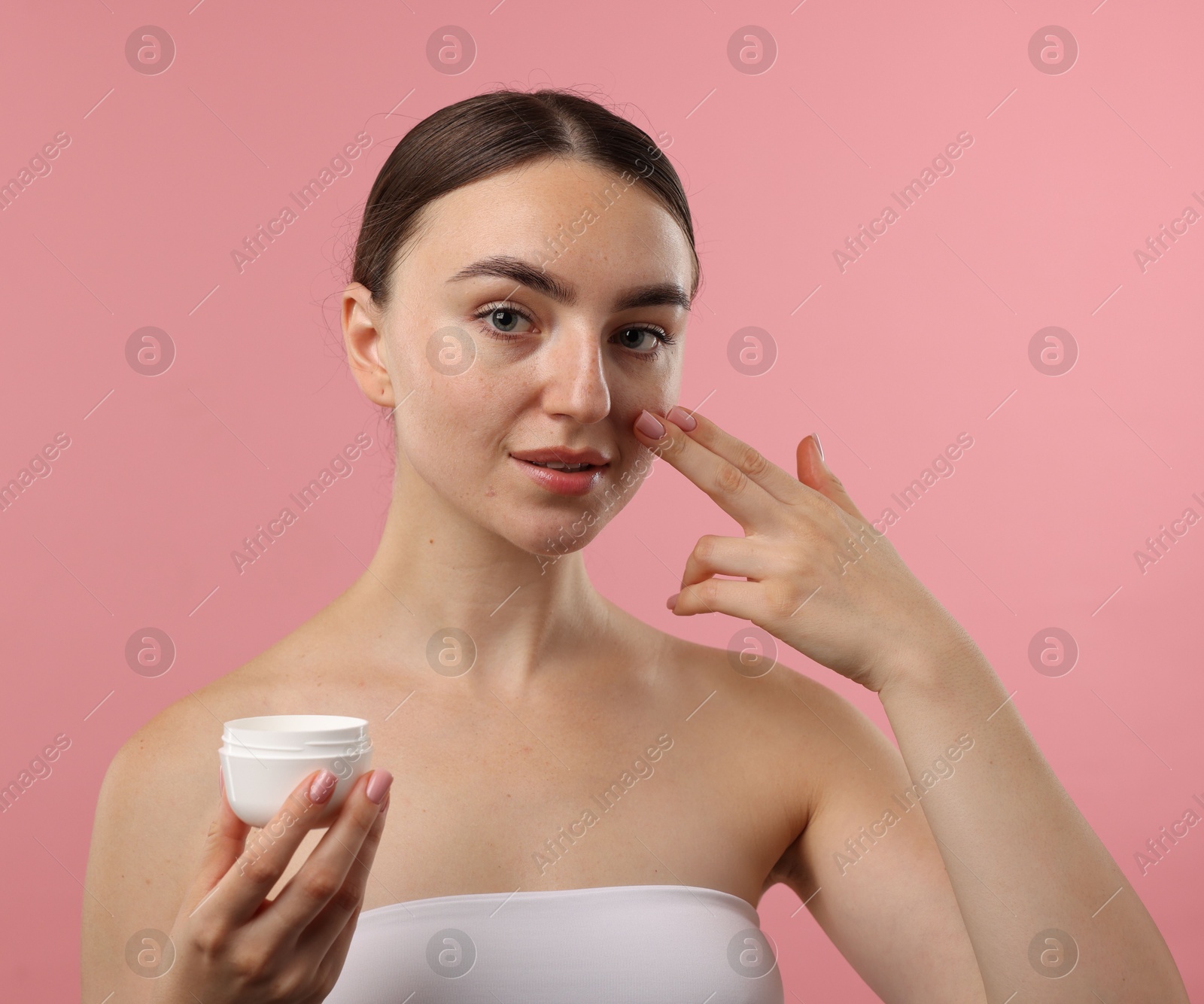 Photo of Beautiful woman applying cream onto her face on pink background