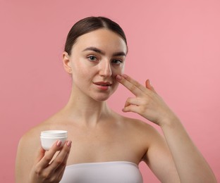 Photo of Beautiful woman applying cream onto her face on pink background