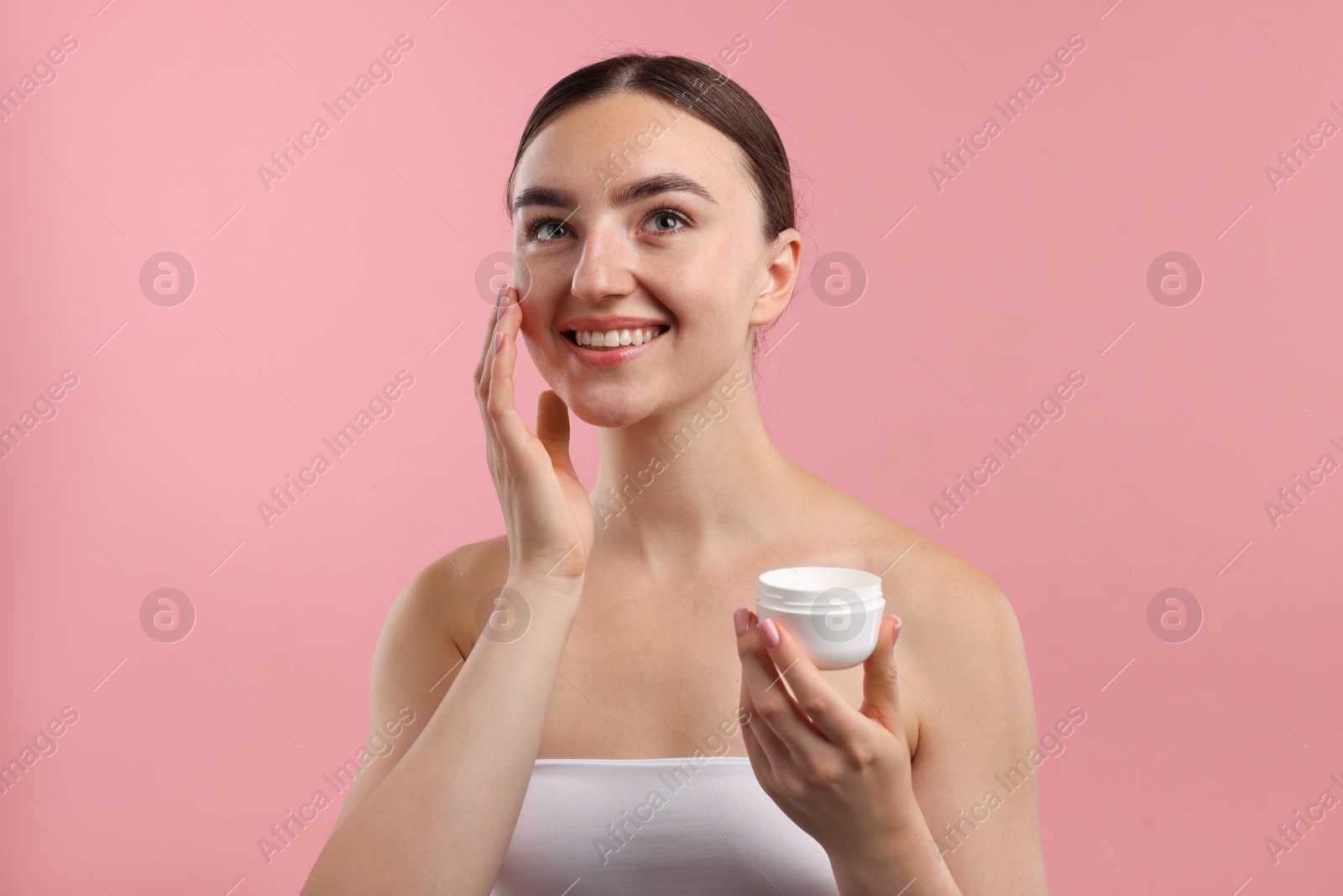 Photo of Beautiful woman applying cream onto her face on pink background