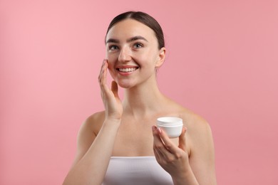 Photo of Beautiful woman applying cream onto her face on pink background