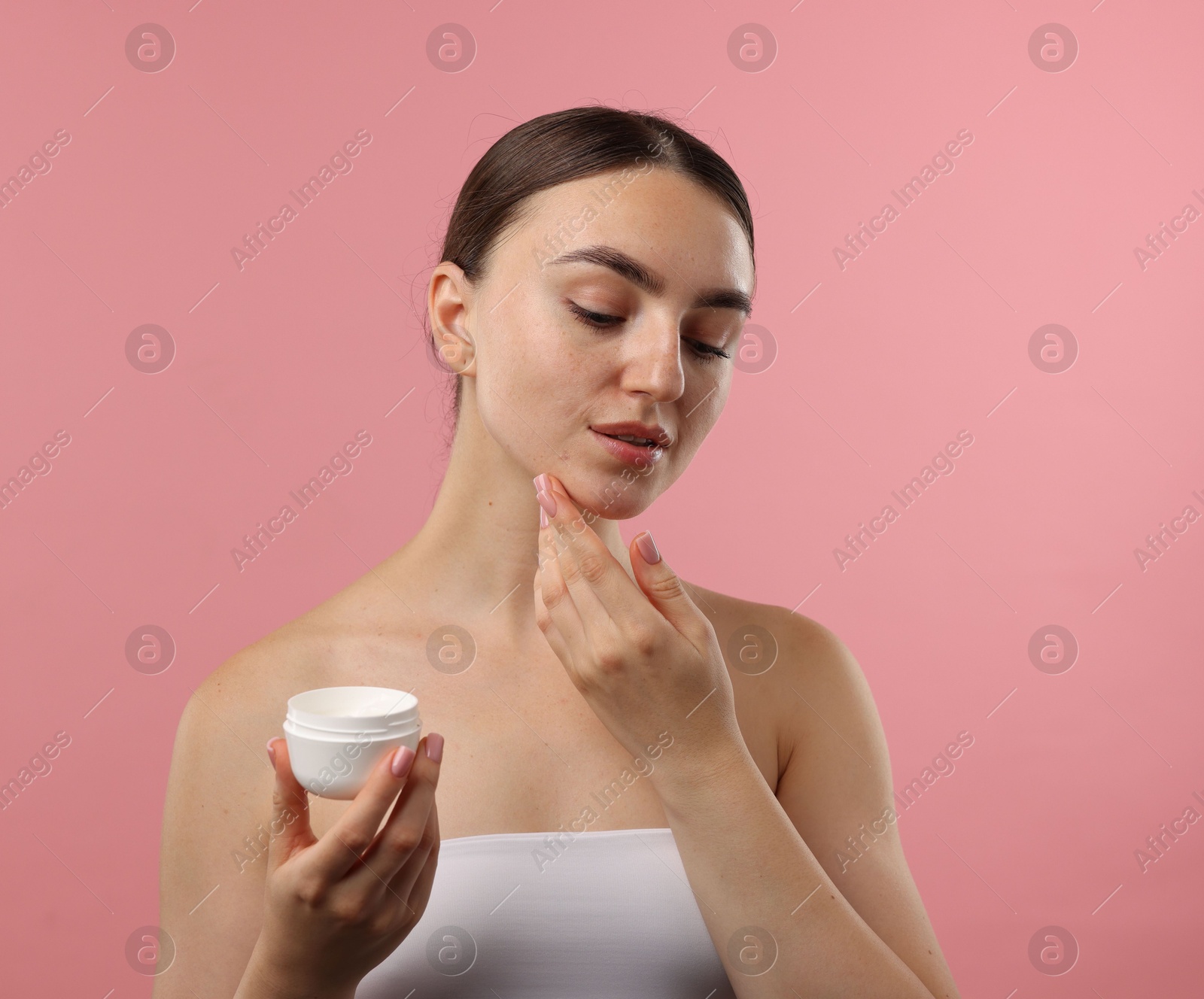 Photo of Beautiful woman applying cream onto her face on pink background