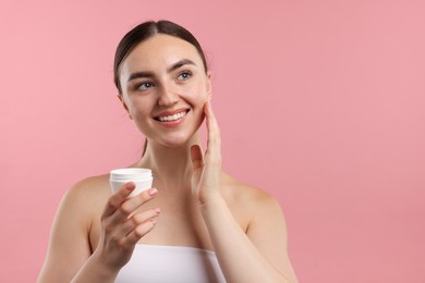 Photo of Beautiful woman applying cream onto her face on pink background. Space for text