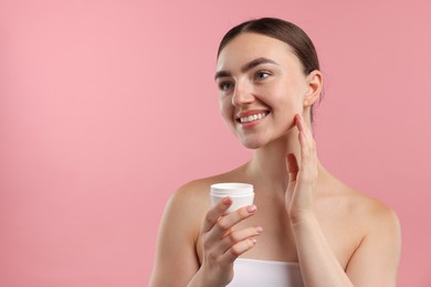 Photo of Beautiful woman applying cream onto her face on pink background. Space for text