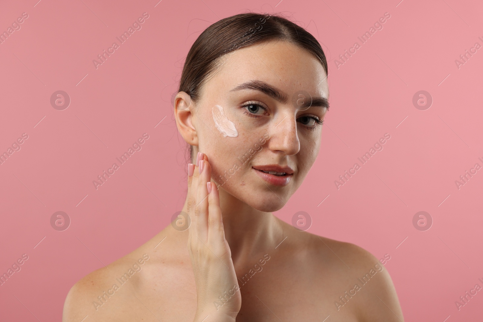 Photo of Beautiful woman with cream on her face against pink background, closeup