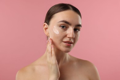 Photo of Beautiful woman with cream on her face against pink background, closeup