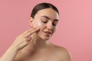 Photo of Beautiful woman applying cream onto her face on pink background