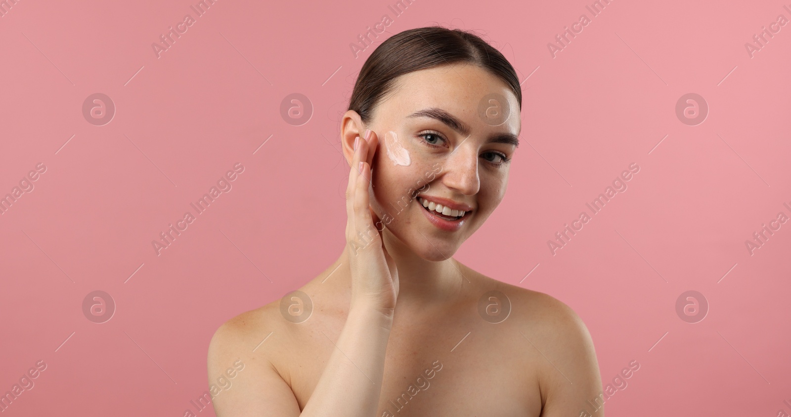 Photo of Beautiful woman applying cream onto her face on pink background