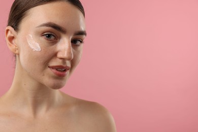 Photo of Beautiful woman with cream on her face against pink background, closeup. Space for text