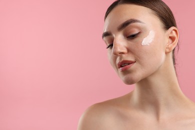Photo of Beautiful woman with cream on her face against pink background, closeup. Space for text