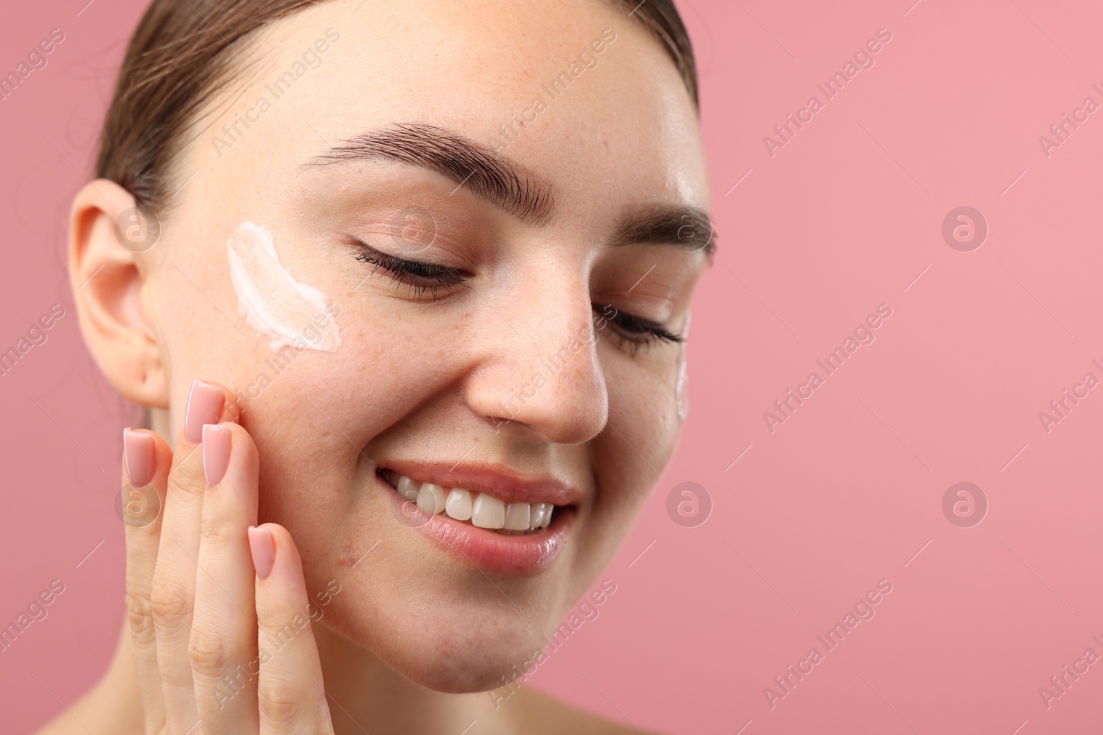 Photo of Beautiful woman with cream on her face against pink background, closeup. Space for text