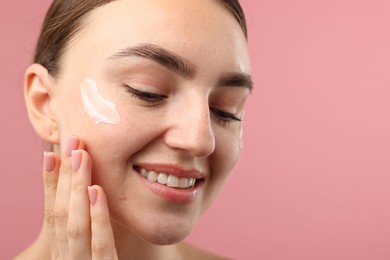 Photo of Beautiful woman with cream on her face against pink background, closeup. Space for text