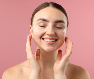Photo of Beautiful woman with cream on her face against pink background, closeup