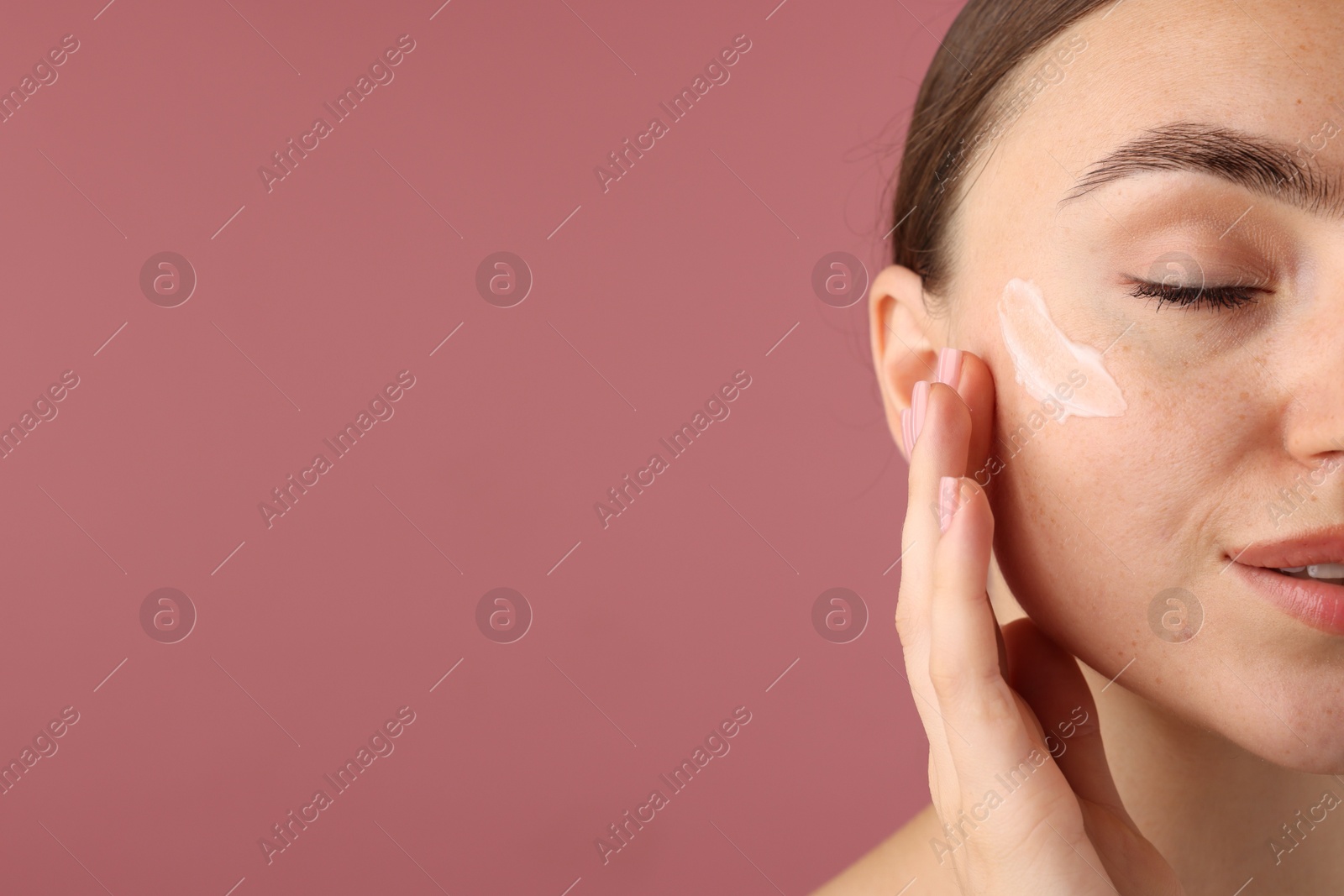 Photo of Beautiful woman with cream on her face against pink background, closeup. Space for text