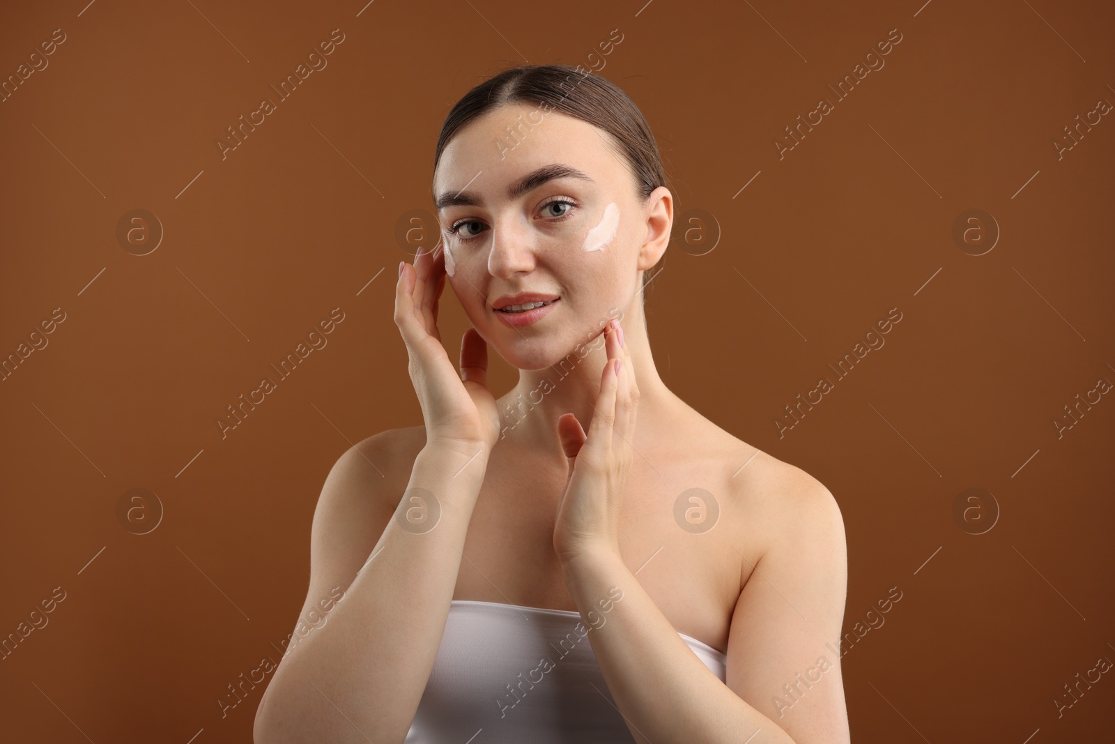 Photo of Beautiful woman with cream on her face against brown background