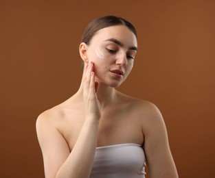 Photo of Beautiful woman with cream on her face against brown background