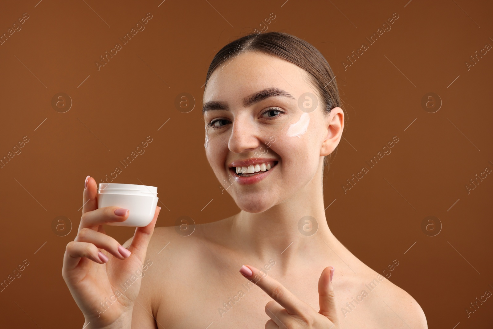 Photo of Beautiful woman with jar of face cream on brown background
