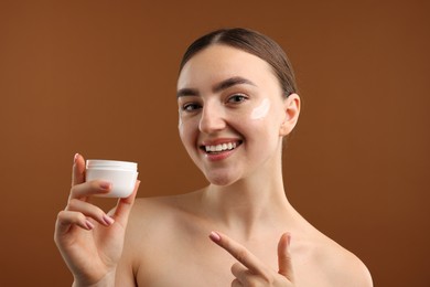 Photo of Beautiful woman with jar of face cream on brown background