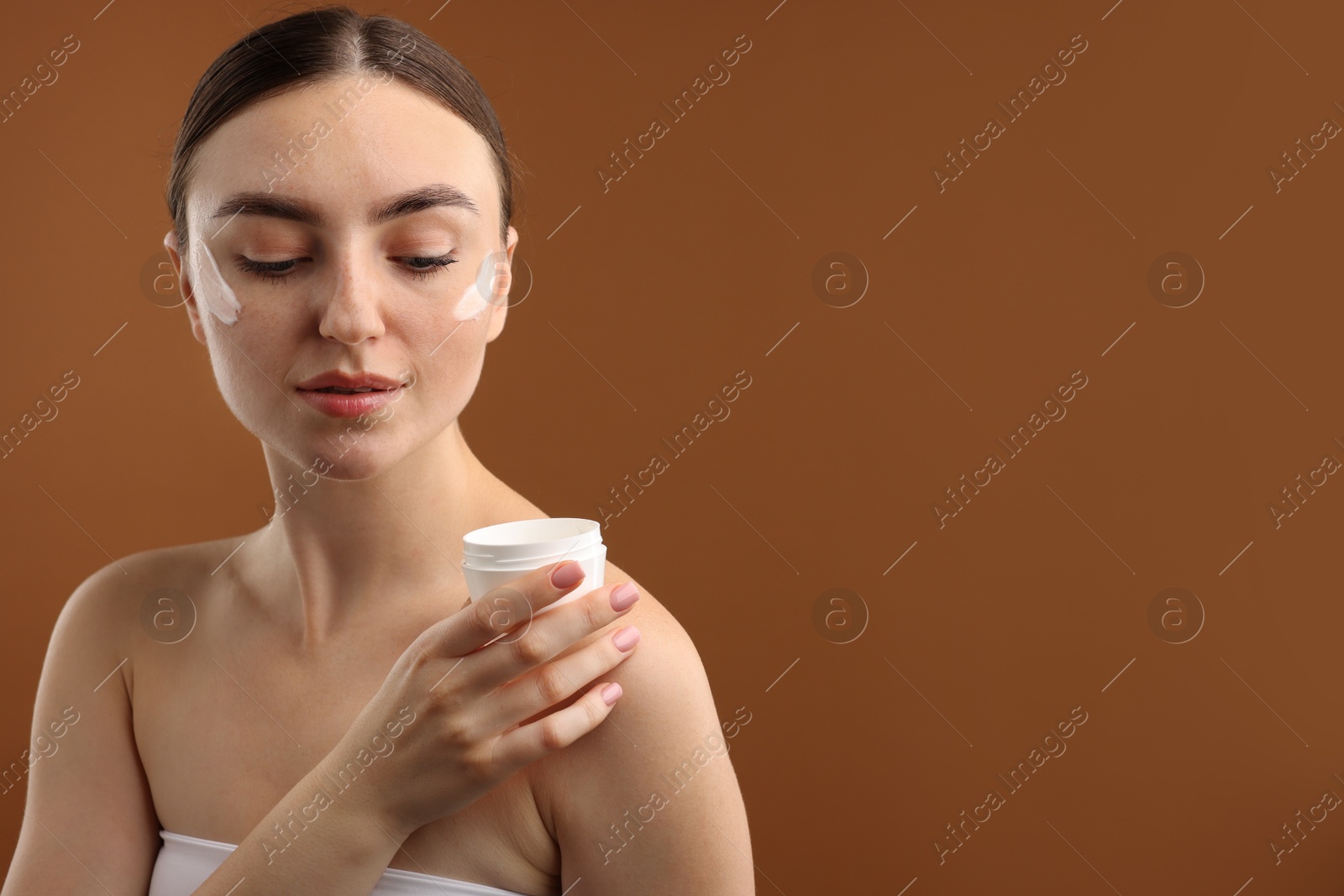 Photo of Beautiful woman with jar of face cream on brown background. Space for text