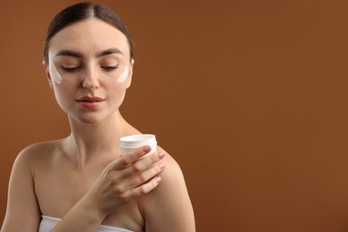 Photo of Beautiful woman with jar of face cream on brown background. Space for text