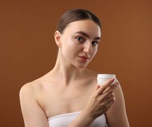 Photo of Beautiful woman with jar of face cream on brown background