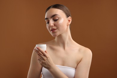 Photo of Beautiful woman with jar of face cream on brown background
