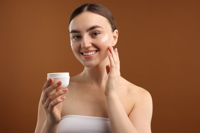 Photo of Beautiful woman with jar of face cream on brown background