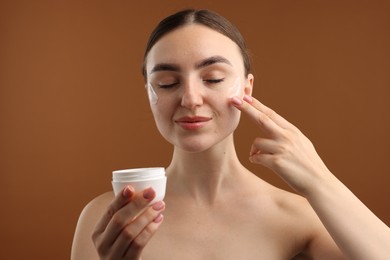 Photo of Beautiful woman applying cream onto her face on brown background